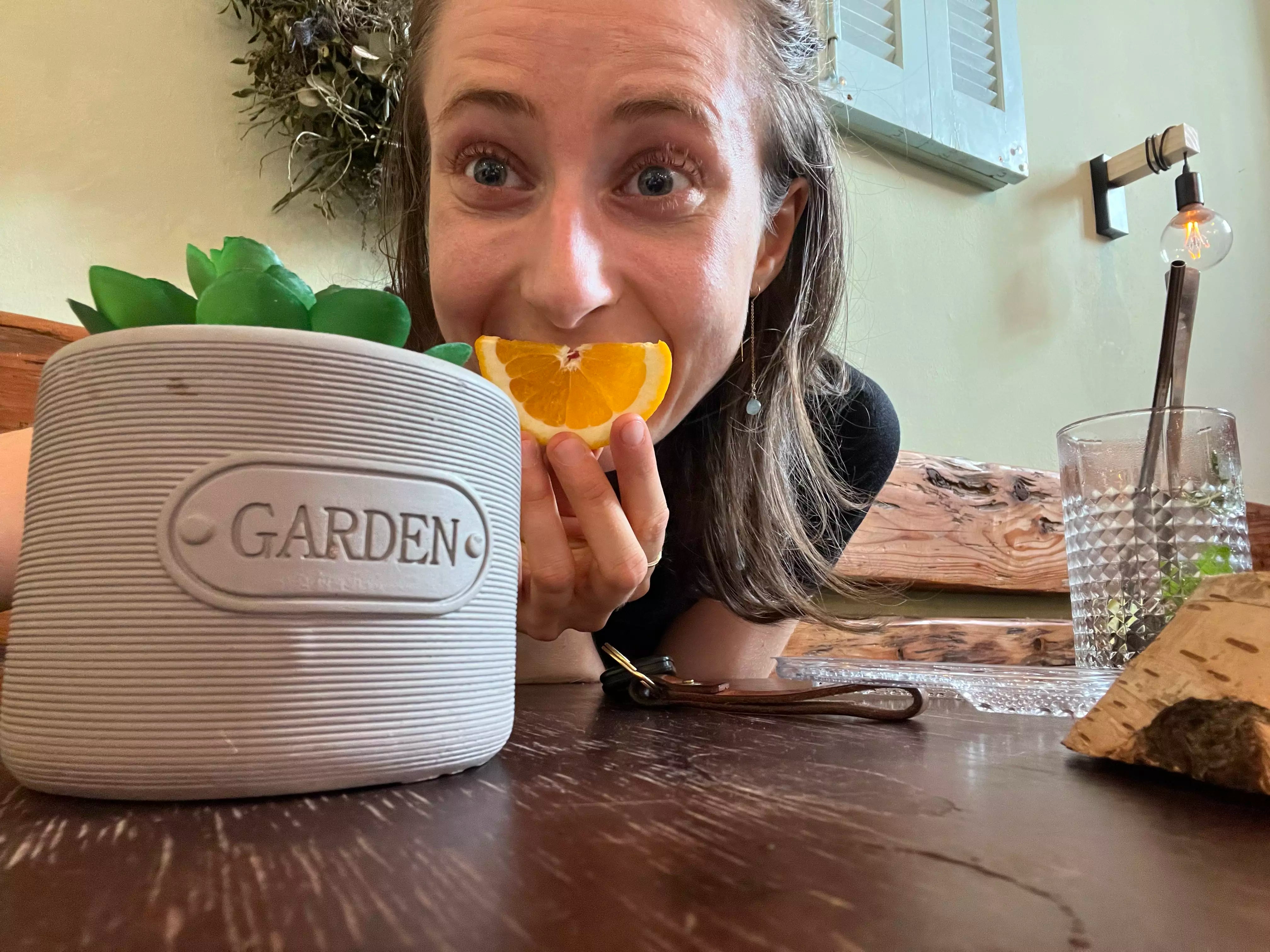 Žena s pomarančom pri kvetináči s nápisom GARDEN
