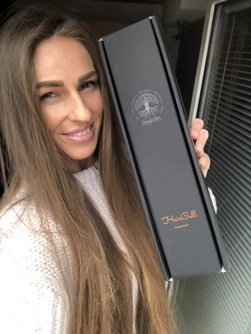 Usmiata zákazníčka s dlhými vlasmi drží balenie HairCell Therapy